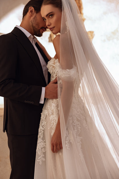 Eine Nahaufnahme des schulterfreien Ärmels von Ariella zeigt zarte Spitzenapplikationen, die der Robe eine luftige, romantische Eleganz verleihen.