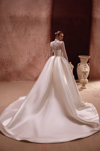 Der Henriette Overskirt mit Spitzenoberteil, langen Ärmeln und Korsettschnürung betont die elegante Silhouette der Braut.