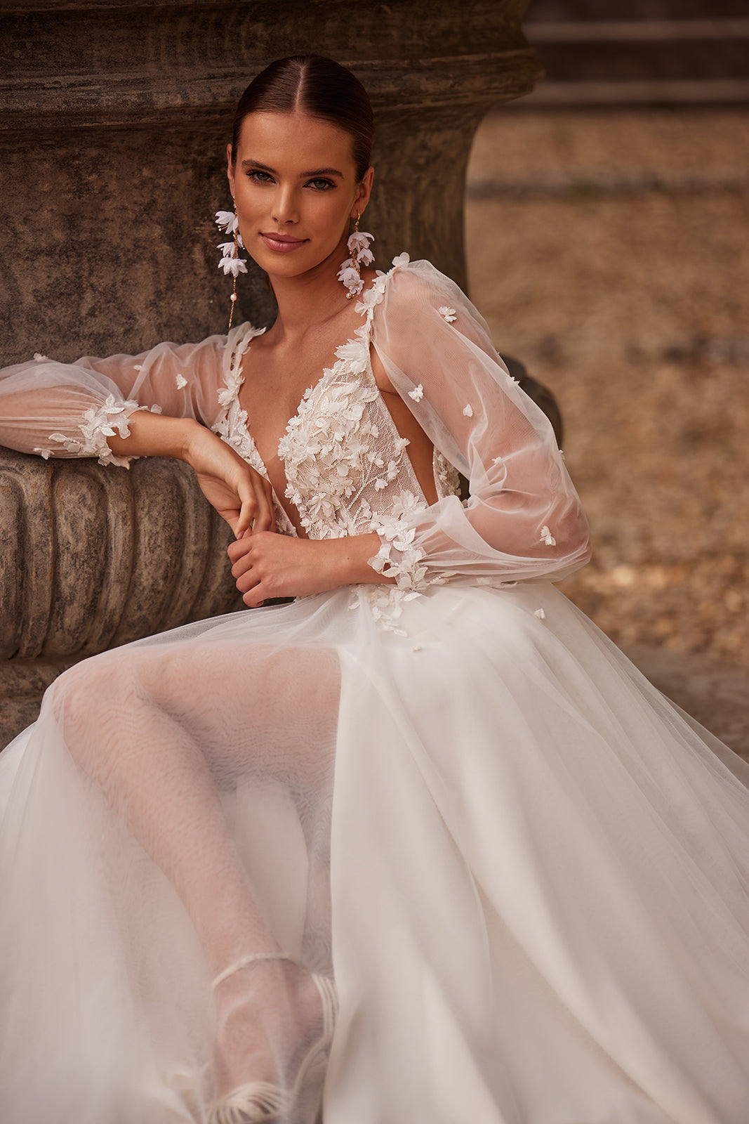 Brautkleid Nozomi: Braut sitzt am Steinsockel, transparente Ärmel und Beinschlitz