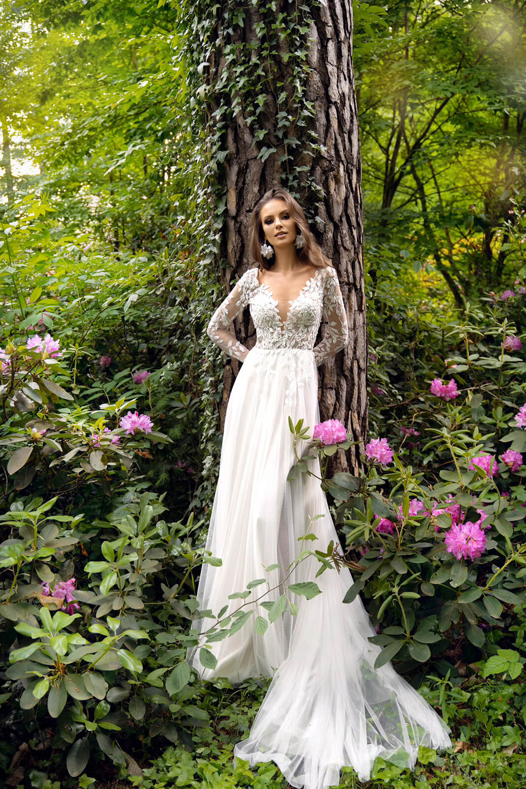 Brautkleid Calista in ganzer Silhouette von vorn, A-Linie aus Tüll vor einem Baumstamm