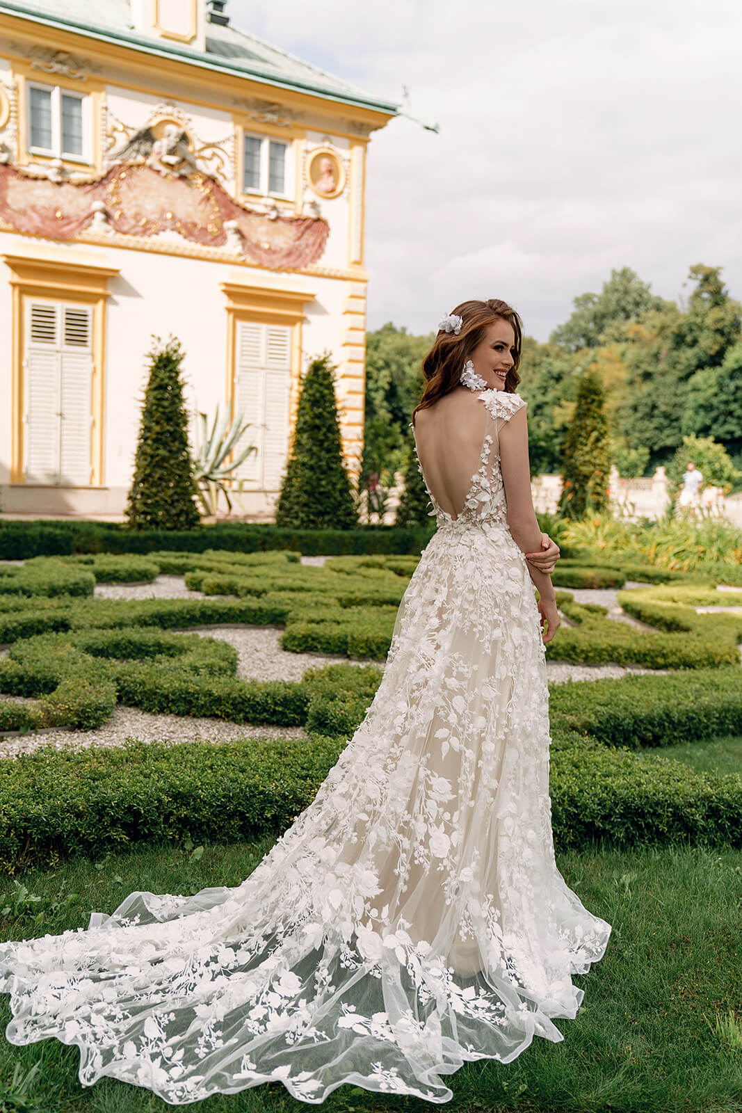 Brautkleid Azalea von hinten im Schlossgarten, Spitzenschleppe auf dem Rasen