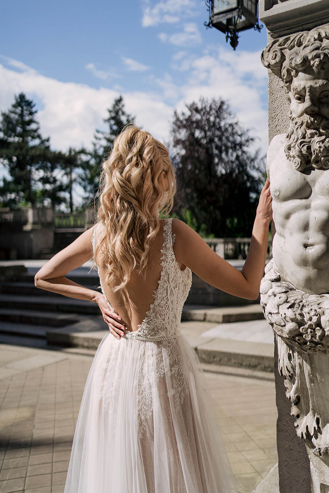 Brautkleid Livia von hinten neben einer Steinfigur, offener Rücken und Tüllrock