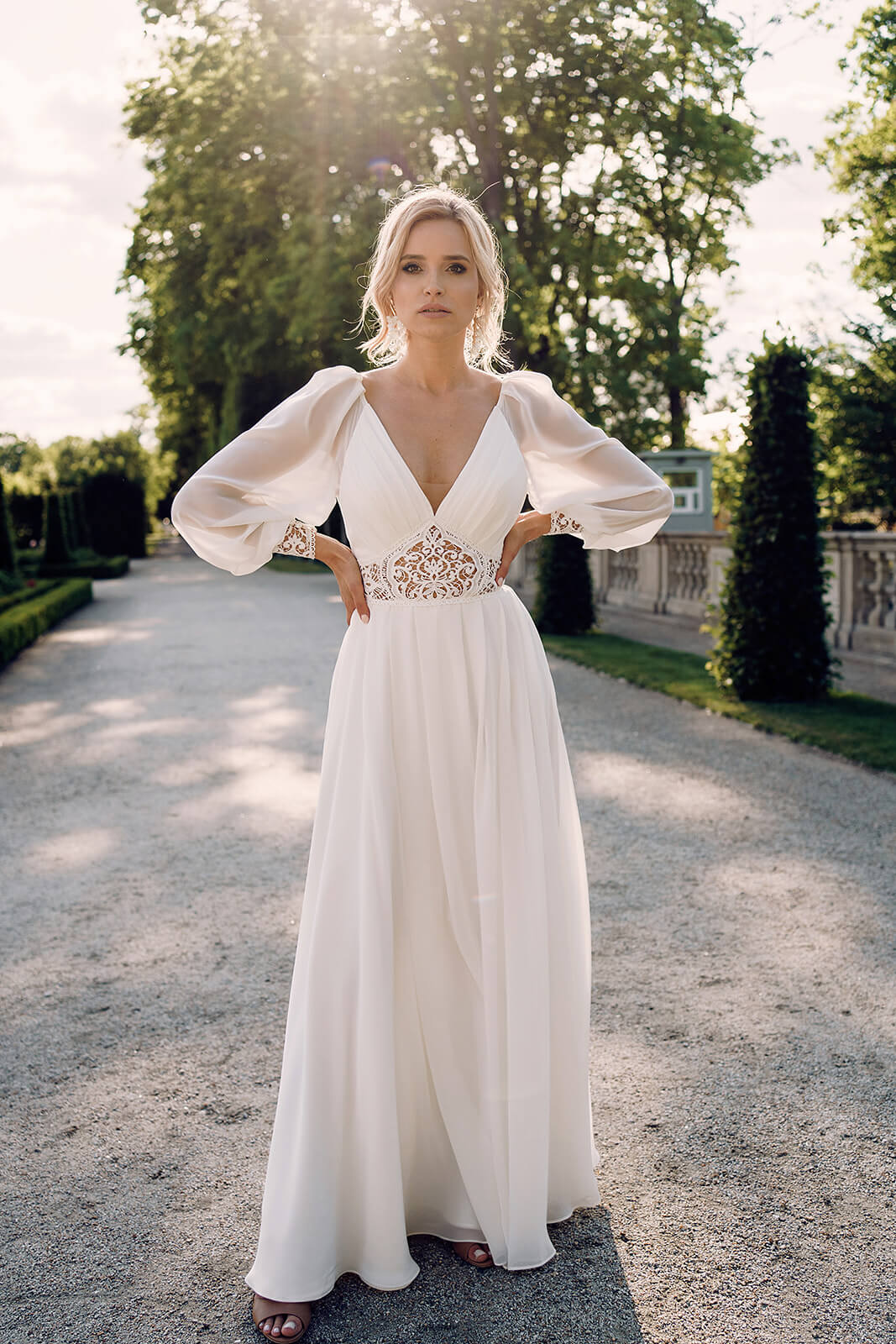 Brautkleid Safona in ganzer Figur in einer Gartenallee, fließender Chiffonrock