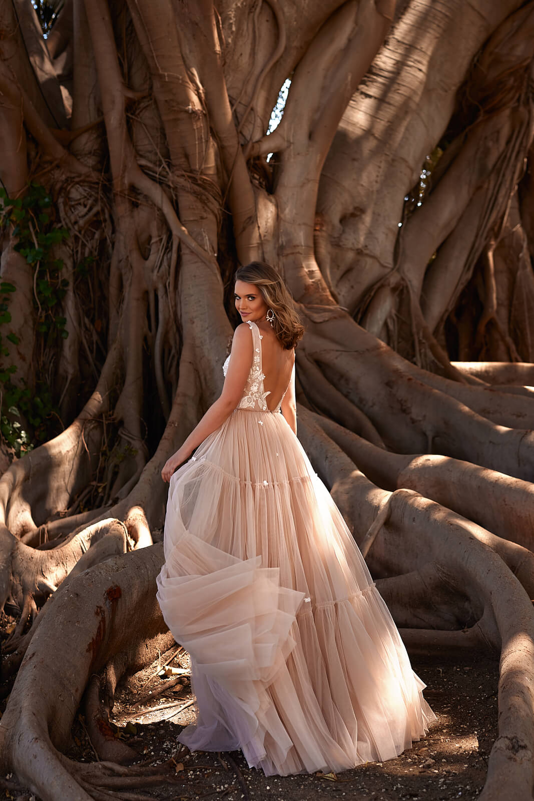Brautkleid Vanessa von hinten, offener Rücken und geraffter Tüllrock, ganze Silhouette am Baum