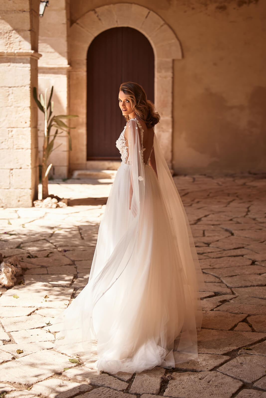 Brautkleid Galadriel in Bewegung, Tüllbahnen und Schleppe vor einem alten Steinportal