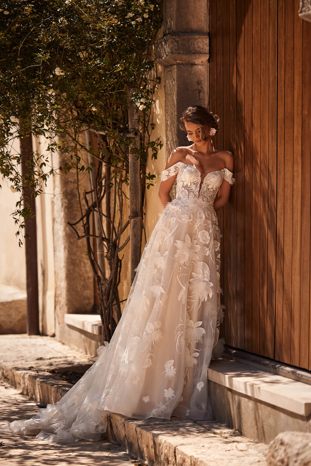 Brautkleid Nenufar von der Seite an einem Holztor, Tüllrock mit Blüten, ganze Silhouette