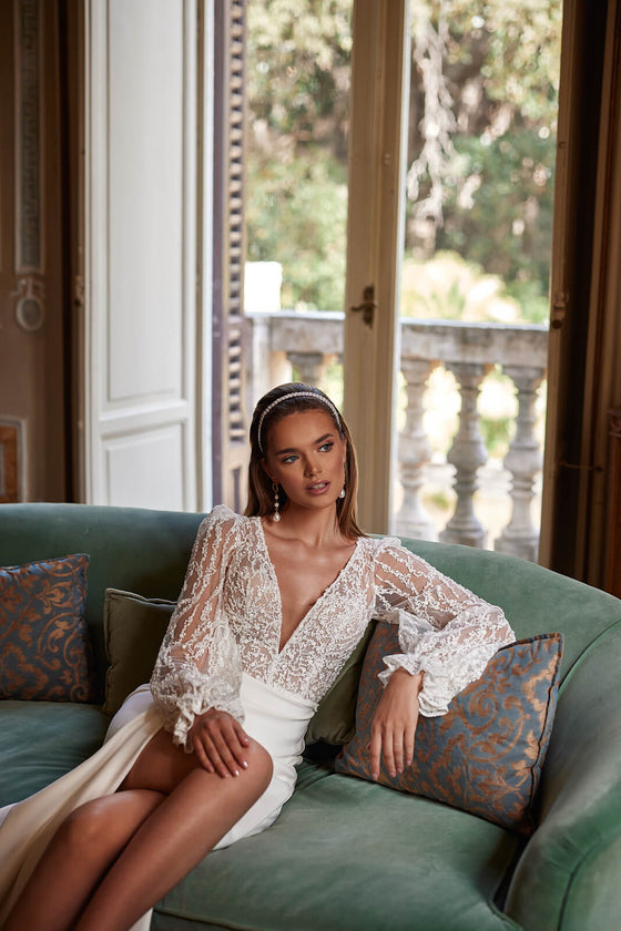 Braut im Kleid Paula auf einem Sofa sitzend, Spitzenärmel und Rock mit hohem Schlitz
