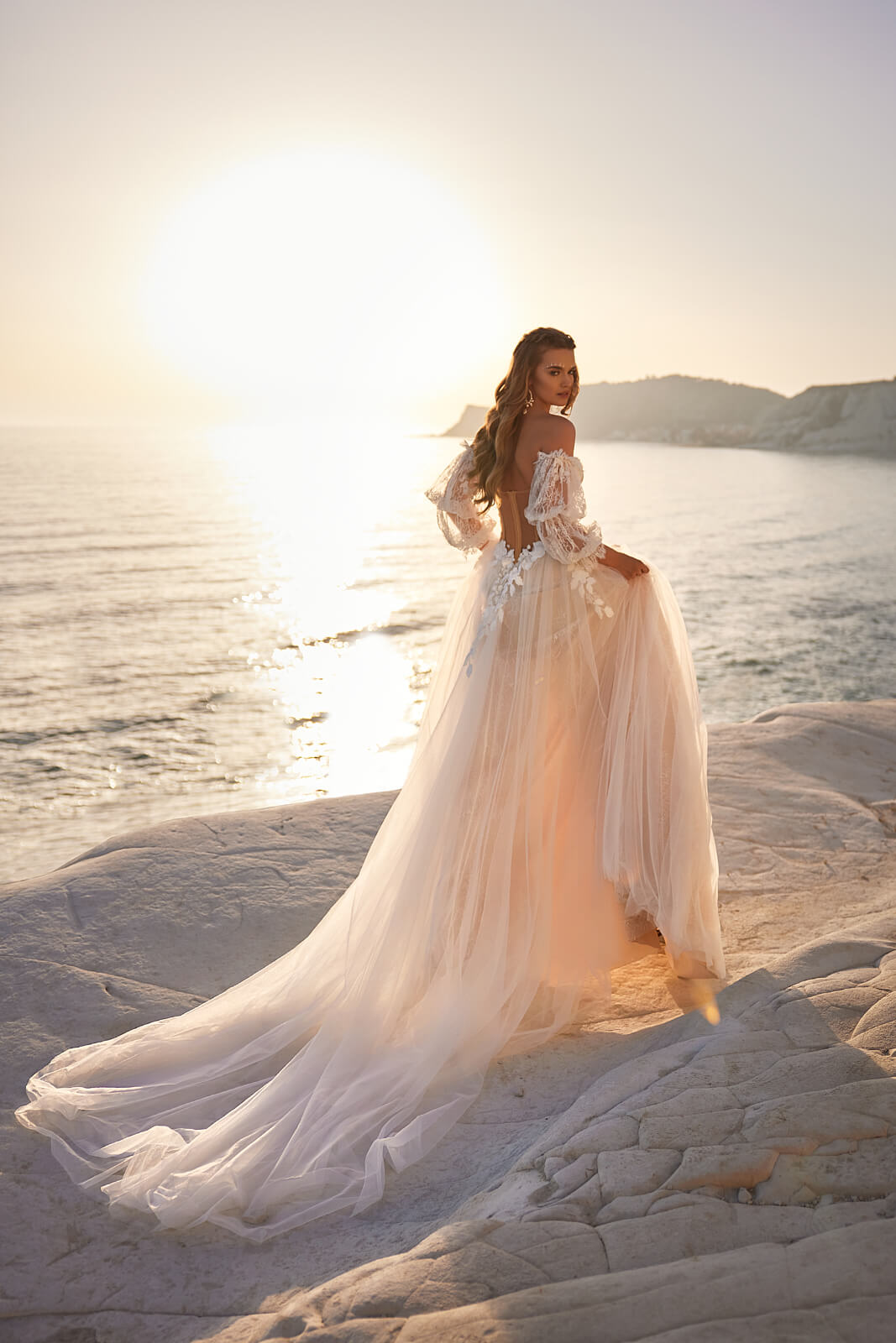 Brautkleid Sievi von hinten mit Tüllschleppe auf den Felsen im Abendlicht