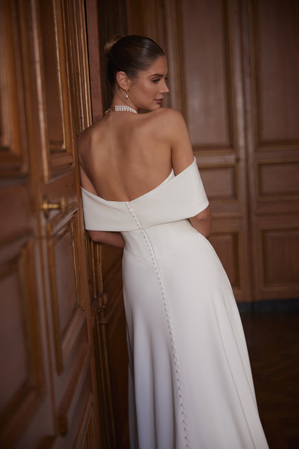 Calliope wedding dress – a wide off-the-shoulder neckline and clean satin skirt with a slit.