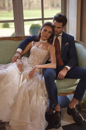 Brautkleid Milkyway auf dem Sofa sitzend neben dem Bräutigam, sternbestickter Tüllrock ausgebreitet