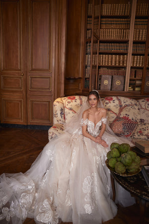 Braut im Brautkleid Vespera mit Schleier auf einem Sofa sitzend, ausgebreiteter Tüllrock mit Blüten