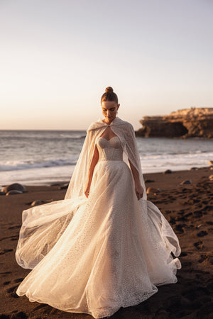 Brautcape Amira weit ausgebreitet über dem Kleid mit Corsage, ganze Figur am Strand
