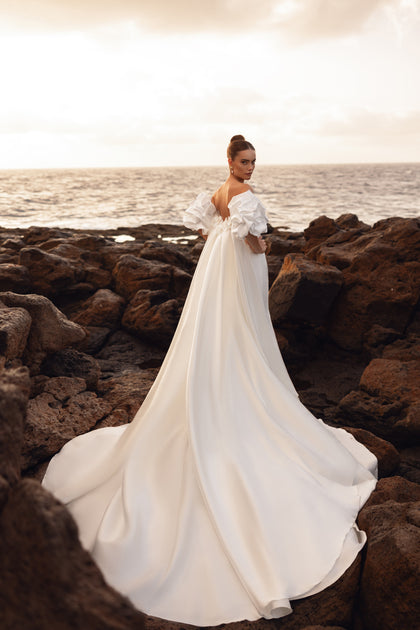 Backless wedding gown with an extra-long train, designed for dramatic seaside bridal portraits.