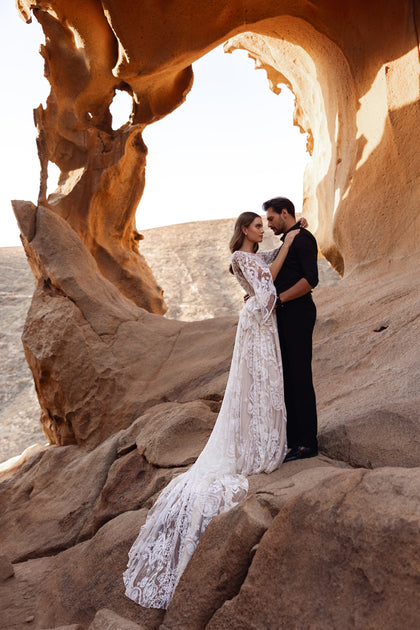 Das Brautkleid Dune mit transparentem Spitzenoberteil und ausgestellten Ärmeln besticht durch feine Stickereien und Boho-Charme.