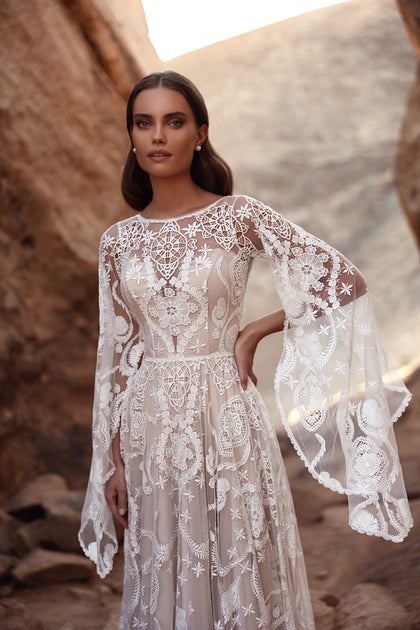 Das Brautkleid Dune mit langer Spitzenschleppe und weiten Ärmeln verkörpert Boho-Romantik in Wüstenkulisse.