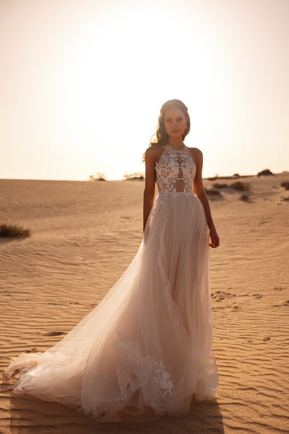 Das Brautkleid Ellie mit transparentem Neckholder-Oberteil und fließendem Tüllrock bezaubert durch zarte Blumenapplikationen.