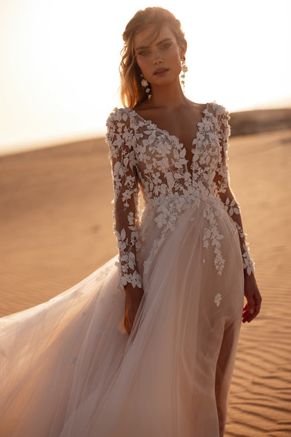 Das Brautkleid Farida mit tiefem V-Ausschnitt und langen Spitzenärmeln begeistert durch zarte 3D-Blumenapplikationen und leichten Tüll.