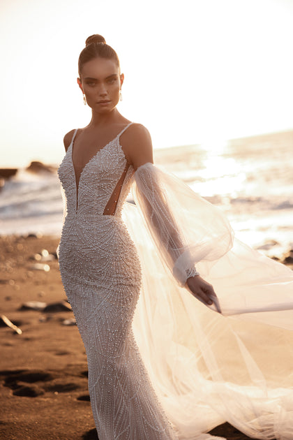 Brautkleid Rebecca im Meerjungfrauenstil mit feinen Trägern und Perlenverzierung strahlt luxuriösen Glanz im goldenen Sonnenuntergang aus.