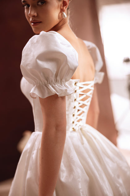 Das kurze Brautkleid Daphne mit Herzausschnitt und Puffärmeln strahlt feminine Anmut und moderne Eleganz aus.