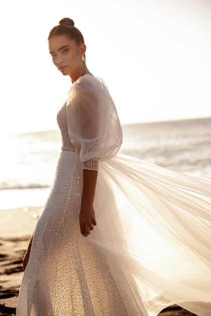 Das Brautkleid Davina mit glitzerndem Stoff und Puffärmeln strahlt feminine Anmut und Glamour aus.