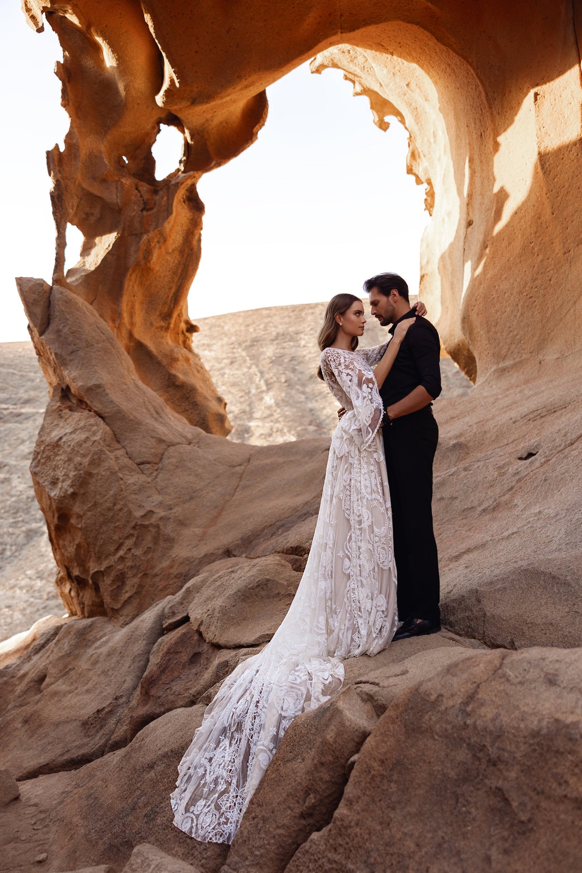 Brautkleid Dune in ganzer Länge unter dem Sandsteinbogen, Braut und Bräutigam in der Wüste