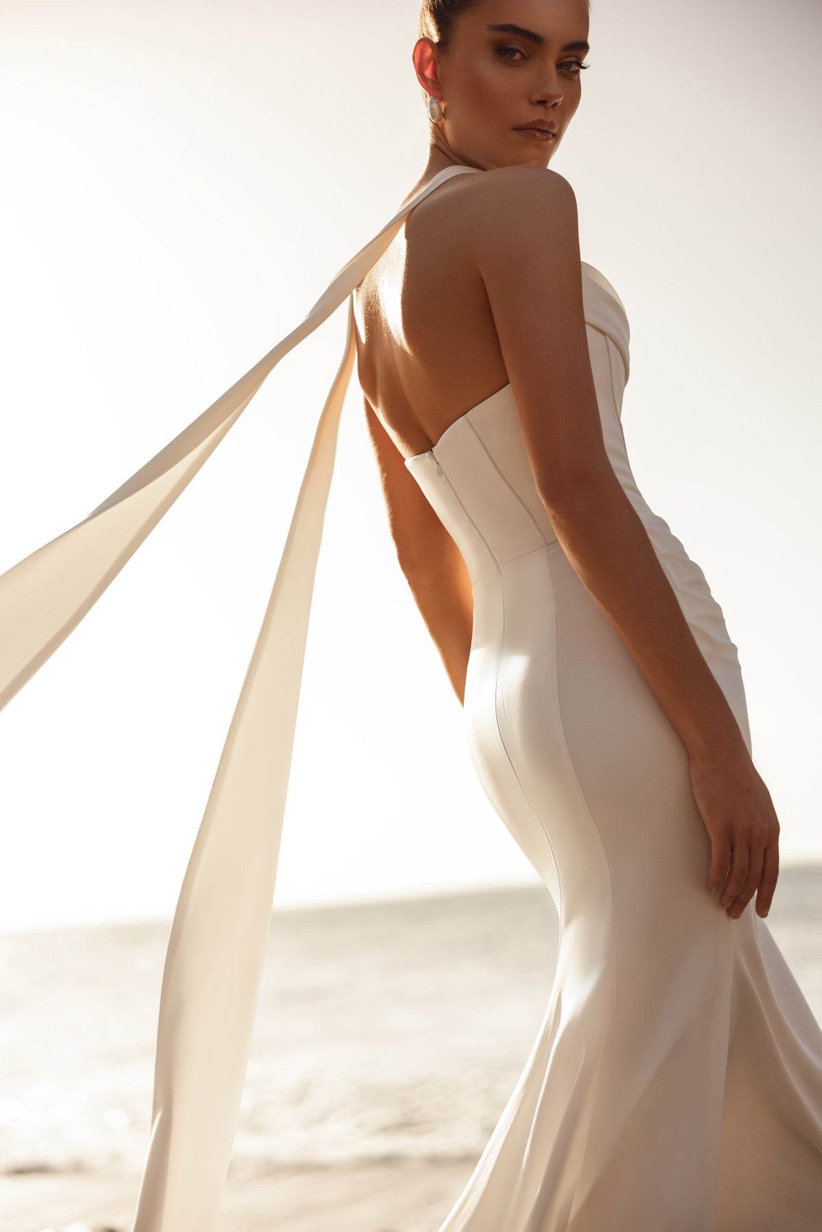 Brautkleid Luna von hinten, lange Schleppe und wehende Satinbänder am Meer