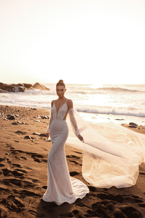 Figurbetontes Meerjungfrau-Brautkleid mit tiefem V-Ausschnitt und langem, fließendem Schleier am Strand.