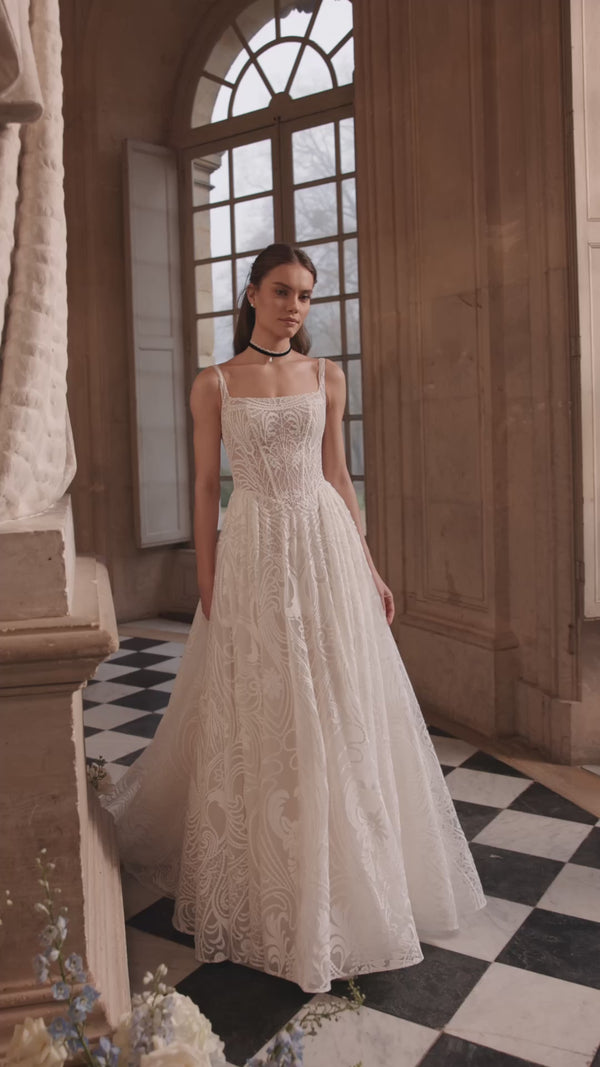 Video of the Frigga wedding dress in motion – A-line silhouette with slender straps, a squared neckline and graphic lace ball skirt.