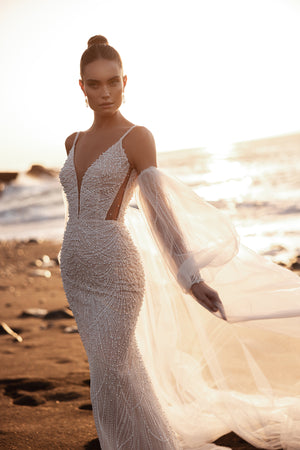 The Rebecca mermaid wedding dress with spaghetti straps and pearl beadwork glows under the sunset, creating a timeless beach bridal look.