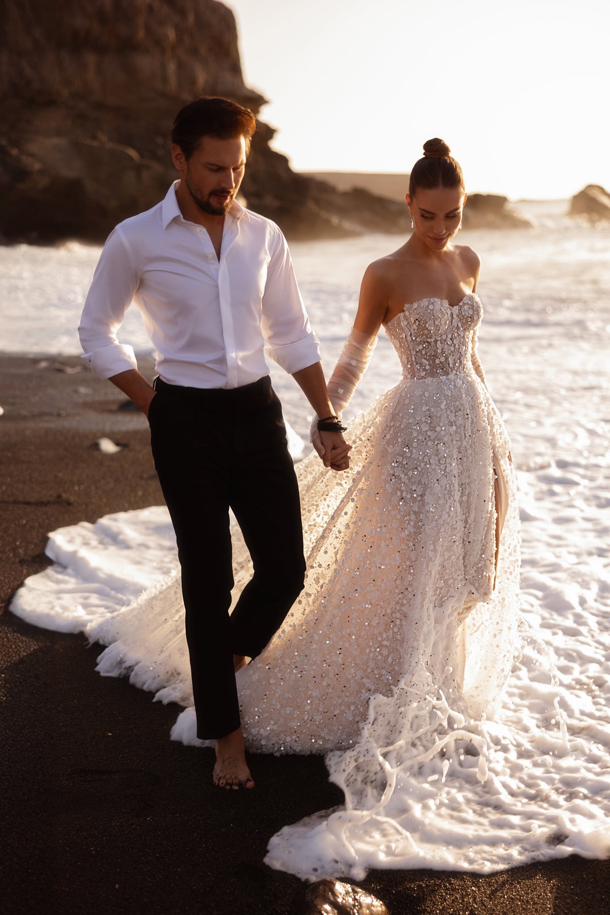 The Reem wedding gown with a beaded corset and front slit shines with thousands of sequins, creating a breathtaking beach bridal look.
