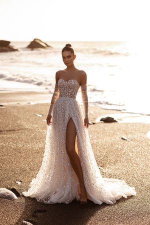 Brautkleid Reem von vorn im Gegenlicht, hoher Beinschlitz und funkelnde Stickerei