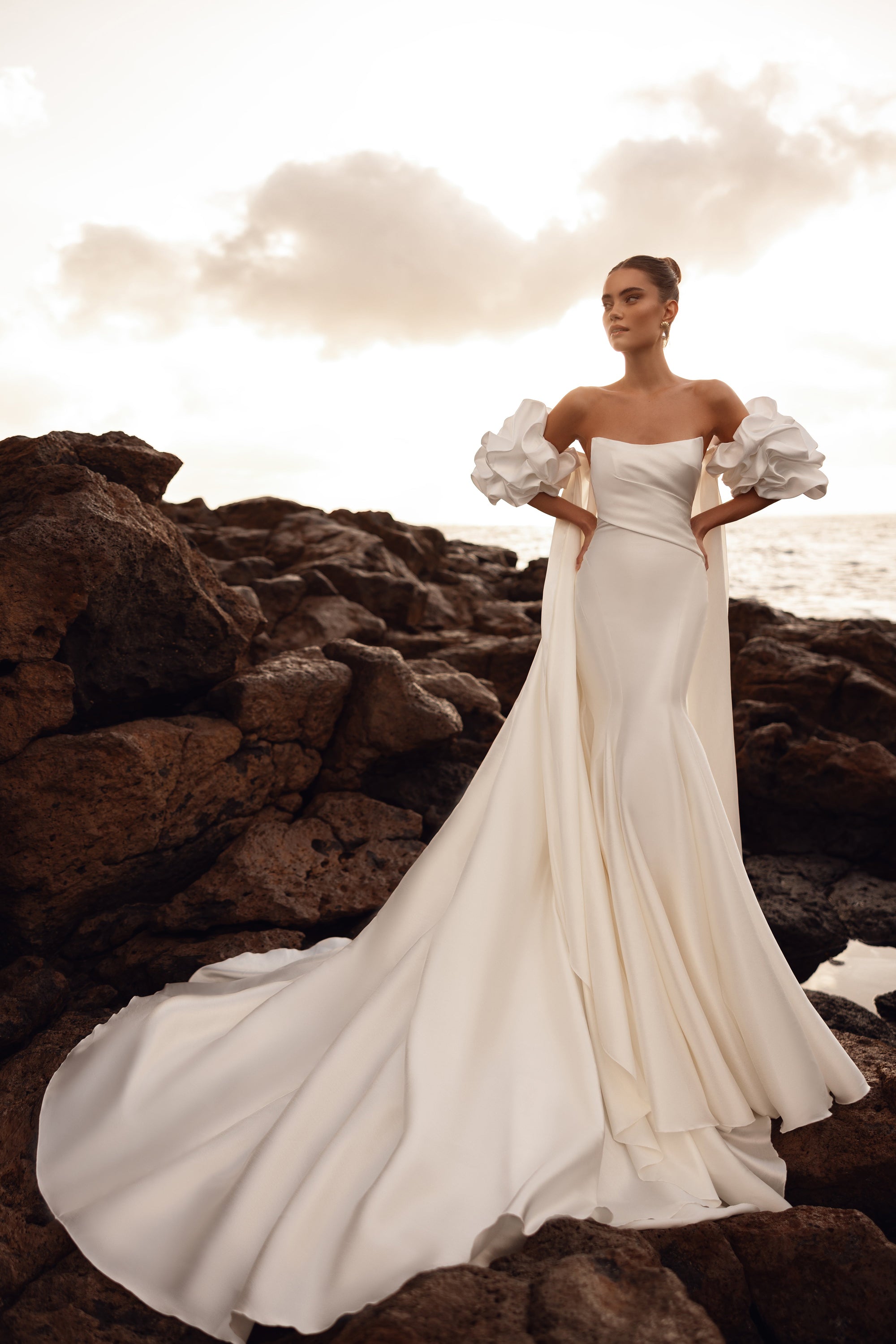 The Soraya wedding dress with dramatic puff sleeves and a long train exudes royal elegance by the seaside.