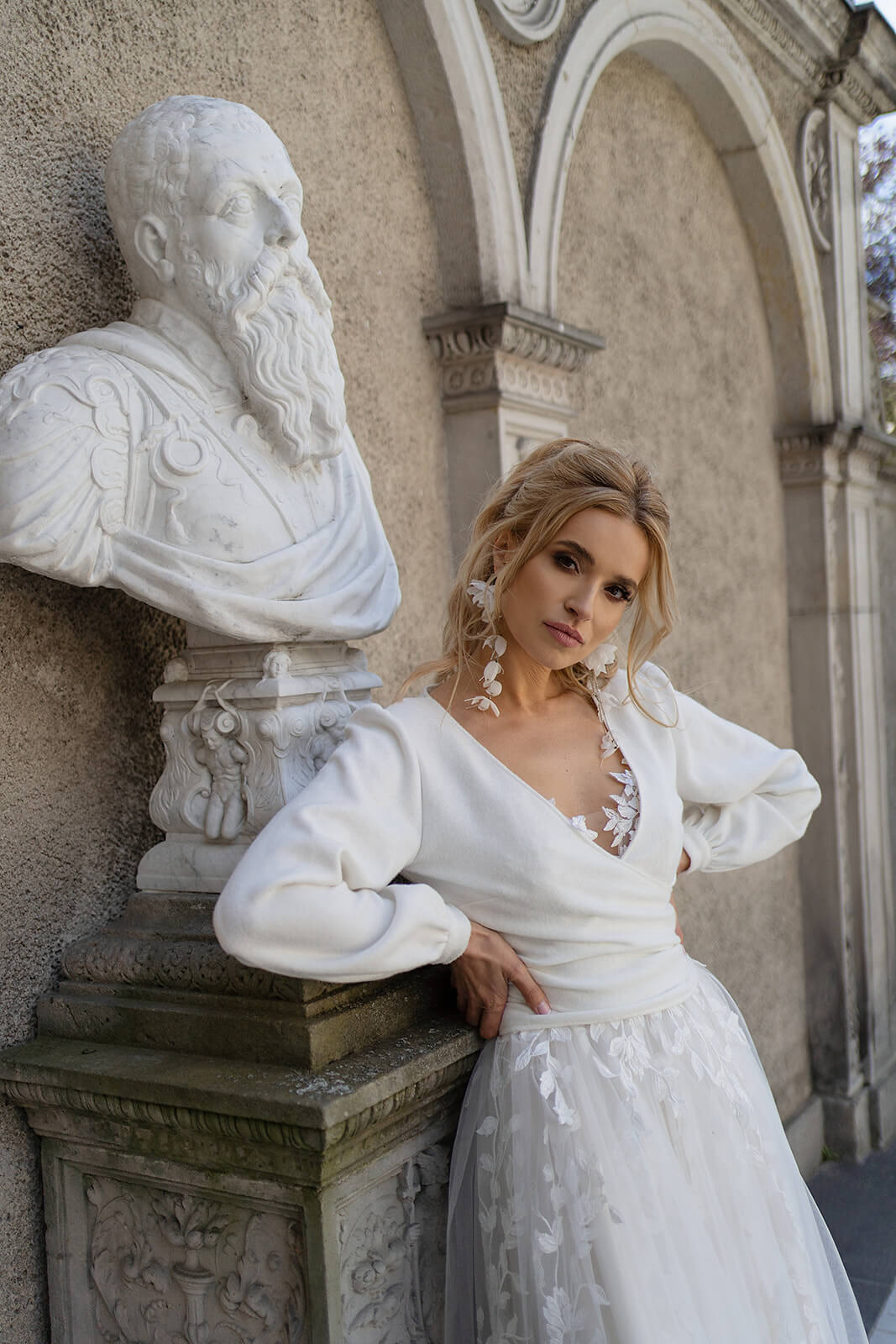 Brautpullover Plain Front über einem Spitzenkleid in A-Linie, Vorderansicht an einer Steinsäule