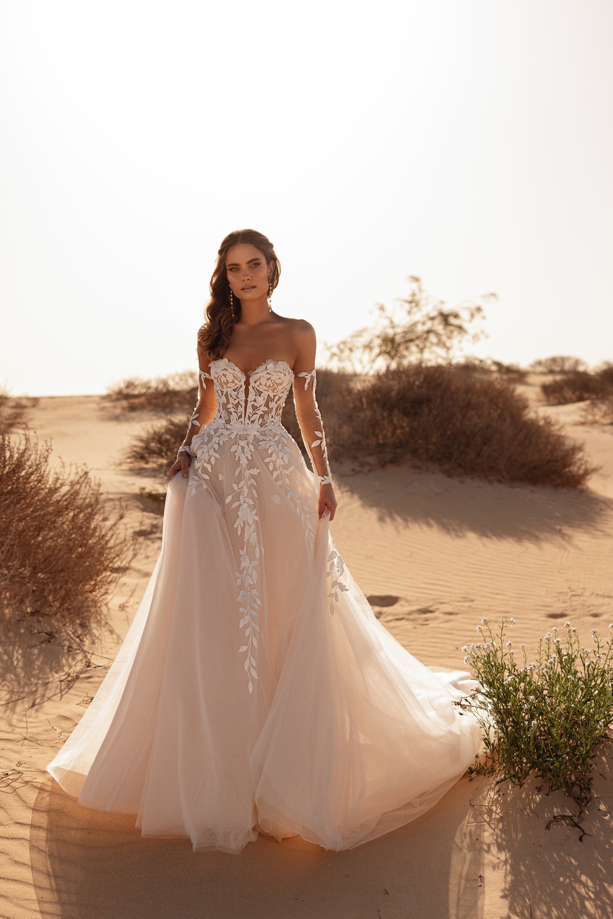 The Tamara wedding dress with off-the-shoulder corset and flowing tulle train radiates romance under the desert sun.